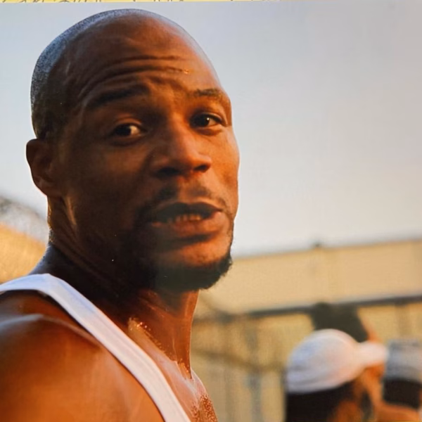 Anthony Hopkins in a white tank top, looking sweaty and intense, with a prison fence in the background.