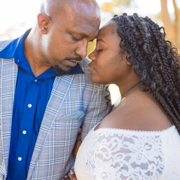A man and woman in a romantic embrace, their foreheads touching, with the woman wearing a white lace top.
