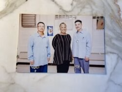 Three people standing together in a hallway; two men in light blue shirts with 'CDCP' on their pants and a woman in a striped top.