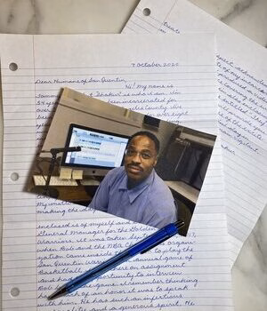 A photograph of a man in a blue shirt sitting at a desk with a computer monitor, placed on top of handwritten notes dated September 2020.