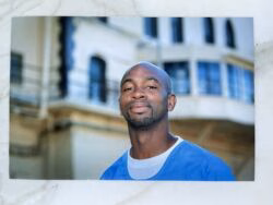 Portrait of a bald Black man with a goatee, wearing a blue shirt, looking directly at the camera with a slight smile.