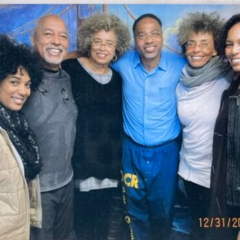 Six people of diverse ages and backgrounds smiling and posing together in front of a blue backdrop.