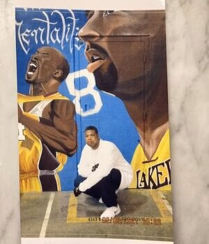 A person crouches in front of a large mural of Kobe Bryant in his Lakers jersey.