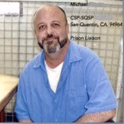 Michael, a man with a mustache wearing a white cap and blue shirt, looks upward outdoors.