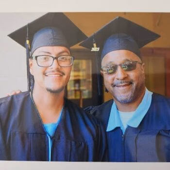 Graduation Day Celebration Two men in blue graduation gowns and caps, one wearing glasses and the other sunglasses, smiling for a photo.