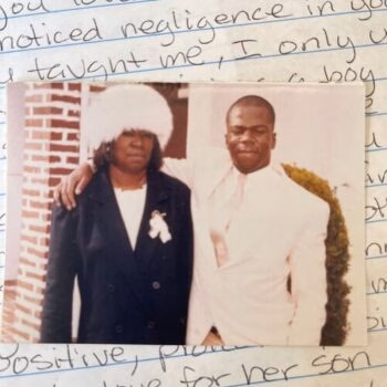 A man and woman in formal attire stand together, with the woman's arm around the man's shoulder.