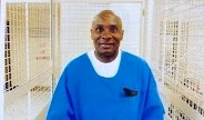 Gregory W. stands in a blue medical gown in a hallway lined with white medical cabinets.
