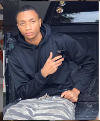 William 'Romeo' sits in the bed of a truck, holding a smartphone and looking at the camera.