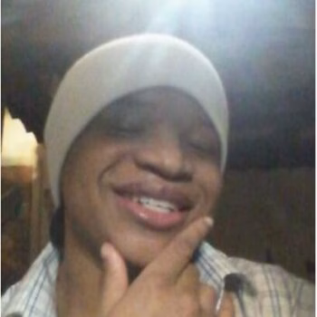 Courtney smiling with eyes closed, wearing a white beanie and plaid shirt, hand on chin.