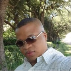 A man named Courtney wearing sunglasses and a checkered shirt, standing outdoors in a sunlit park.