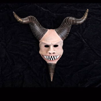 A grotesque mask with two large, curved horns and a long, pointed nose, featuring a wide, toothy grin, set against a black background.