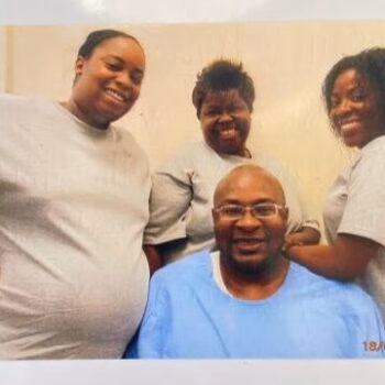 Four smiling people, three women and one man, posing together indoors.