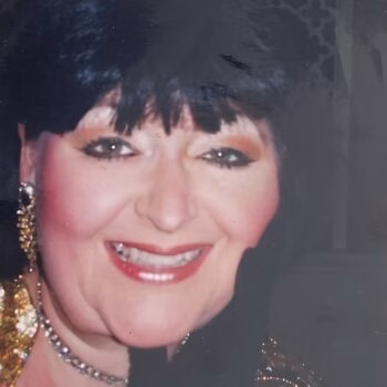Aharon006 (1) Portrait of Aharon, a smiling woman with dark hair, wearing a gold sequined top, a necklace, and earrings.