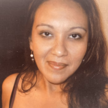 Rosanna, a woman with long dark hair and a pearl earring, smiles at the camera.