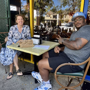 Jerry and a woman sit at an outdoor cafe table, smiling and gesturing.