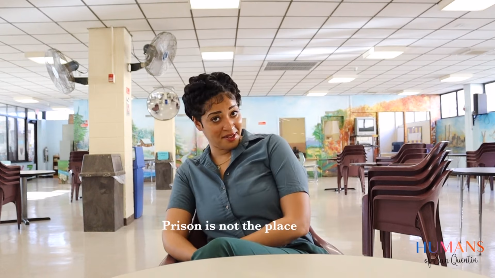 Kimberly, 34, sits in a large, empty room with stacked chairs, looking at the camera with the text 'Prison is not the place' overlaid.