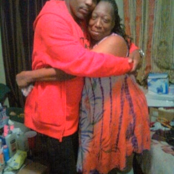David 2 A man in a red hoodie embraces a woman in a patterned dress in a cluttered room.