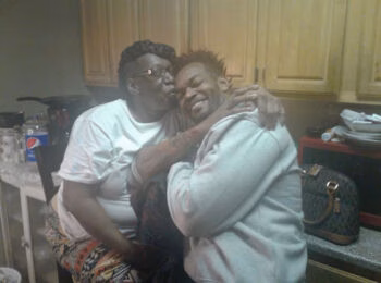 David A woman with glasses and a man embrace in a kitchen, both smiling warmly.