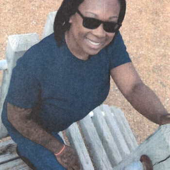 ebony 2 Ebony 2 smiles while sitting on a wooden bench outdoors.