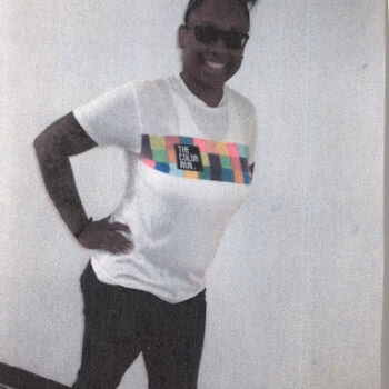 ebony 4 A smiling woman with dark hair in a high ponytail and sunglasses, wearing a white t-shirt with a colorful 'THE COLOR RUN' graphic and black pants.
