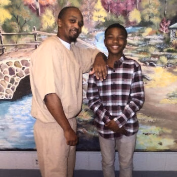 Shak 3 poses with a young boy in front of a landscape mural.