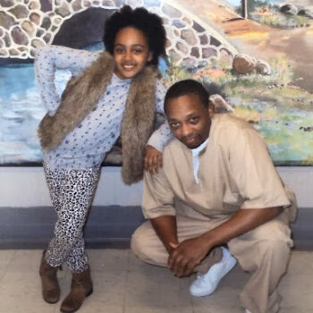 A woman and a man posing together in front of a mural.
