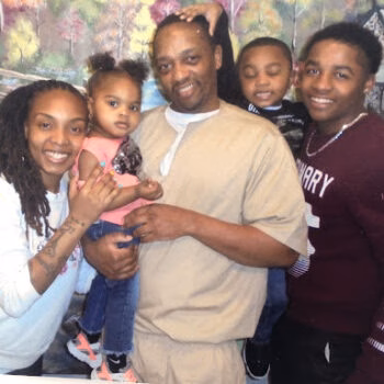 A smiling family of five, including a man, woman, and three children, posing together indoors.