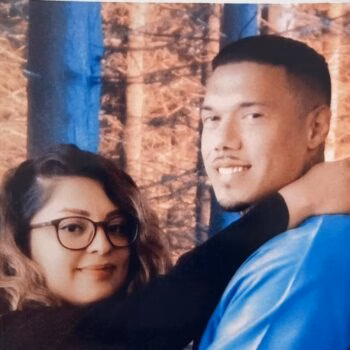 A man and woman posing together in a forest setting.
