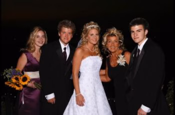 Wedding reception group photo A bride in a white gown stands with four guests at a wedding reception, including a woman in a purple dress holding sunflowers and three men in tuxedos.