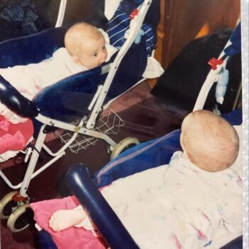 Two babies in strollers Two babies in blue strollers, one looking towards the camera and the other with their back to the viewer.