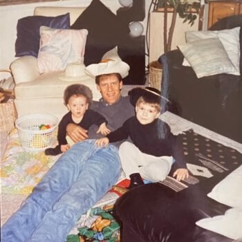 Man and boys in cowboy hats A man wearing a cowboy hat lies on a Teenage Mutant Ninja Turtles blanket with two young boys, one of whom is also wearing a cowboy hat.