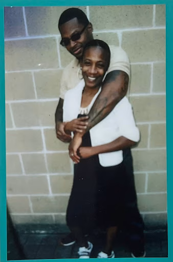 Kareem, 44, smiling and embracing a woman against a brick wall.
