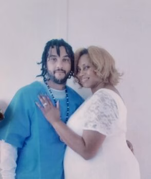 Anthony with his mother Anthony and his mother pose together; he wears a blue shirt and a beaded necklace, while she is in a white lace dress.