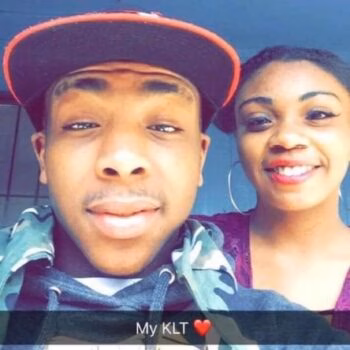 A selfie of a man and a woman. The man wears a red and black cap and a camo hoodie. The woman wears a purple top and large hoop earrings. Text at the bottom reads 'My KLT' with a red heart.