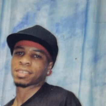 Portrait of Michael Hughes wearing a black hat with a red band, a black shirt, and a blue patterned background.