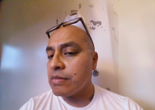 A close-up of a bald man with glasses on his head, wearing a white t-shirt and a large silver earring.