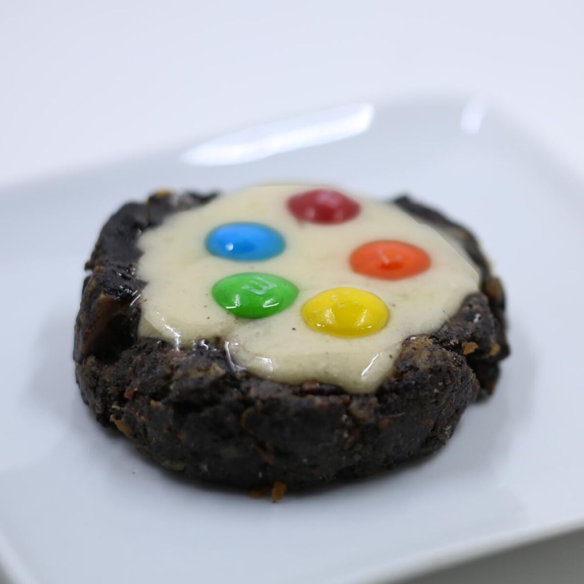 Photo of a dark brown cookie with white icing and topped with colorful M&Ms.