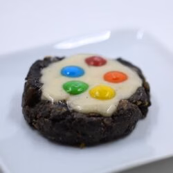Photo of a dark brown cookie with white icing and topped with colorful M&Ms.