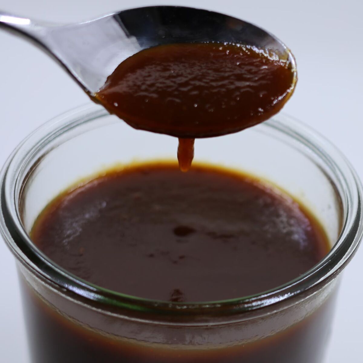 Photo of a spoon dripping barbecue sauce into a jar