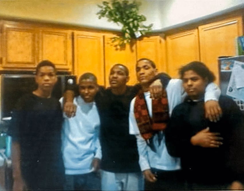 Five young men standing together in a kitchen, with arms around each other's shoulders.