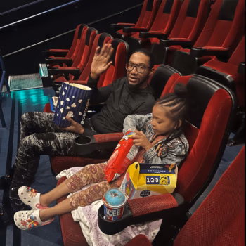 Man and girl in movie theater A man and a young girl are seated in a movie theater, surrounded by snacks like popcorn and ice cream.
