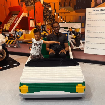Man and Girl in LEGO Car A man and a young girl smile while sitting in a large, colorful LEGO car at a LEGO City exhibit.