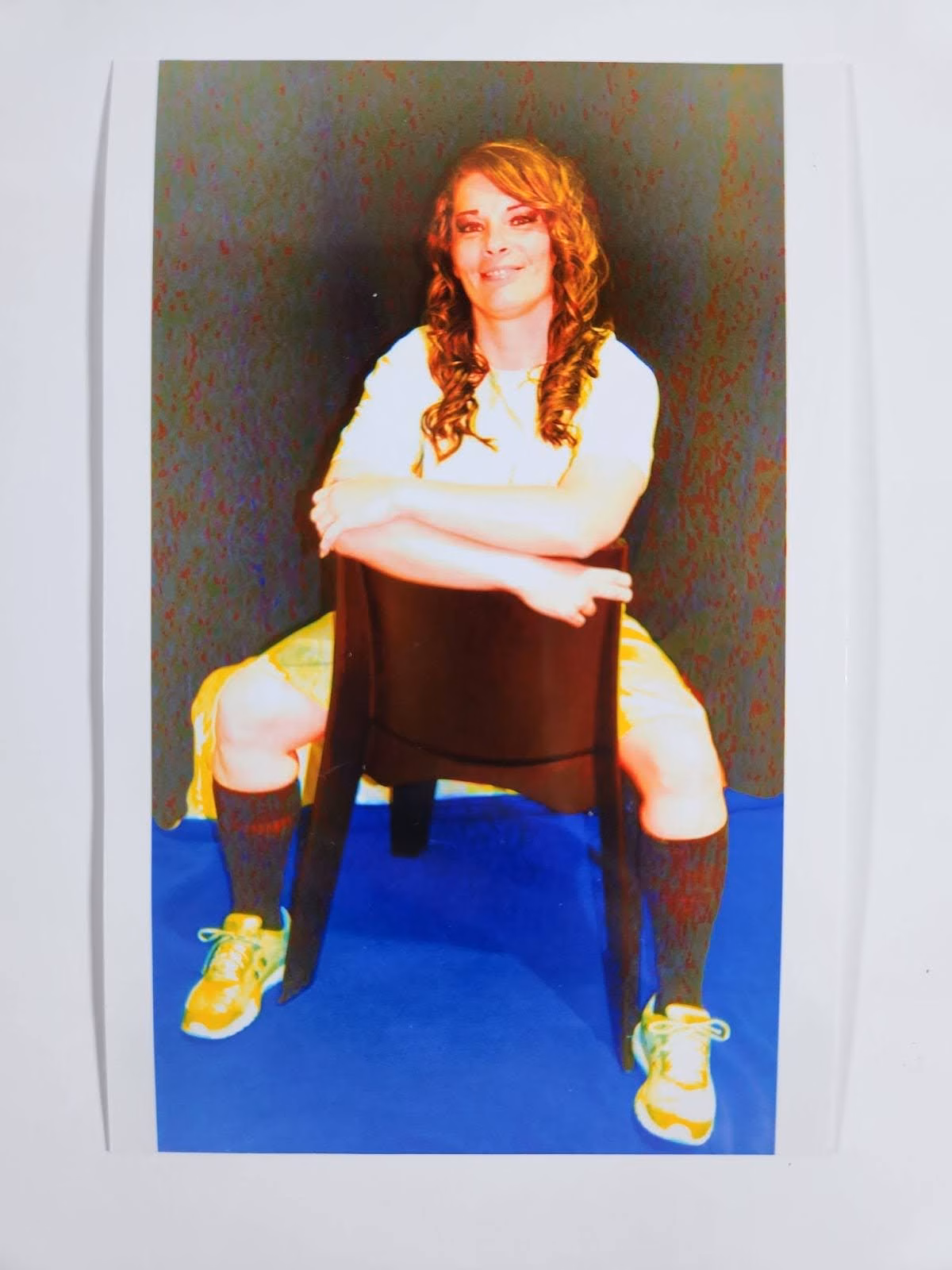 Samantha sits on a chair with arms crossed, wearing a white shirt, yellow shorts, and yellow sneakers.