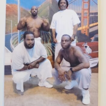 Four men posing in front of a mural featuring the Golden Gate Bridge and a mountain. Two men are crouching in the foreground, one is standing in the back left, and another is standing in the back right.