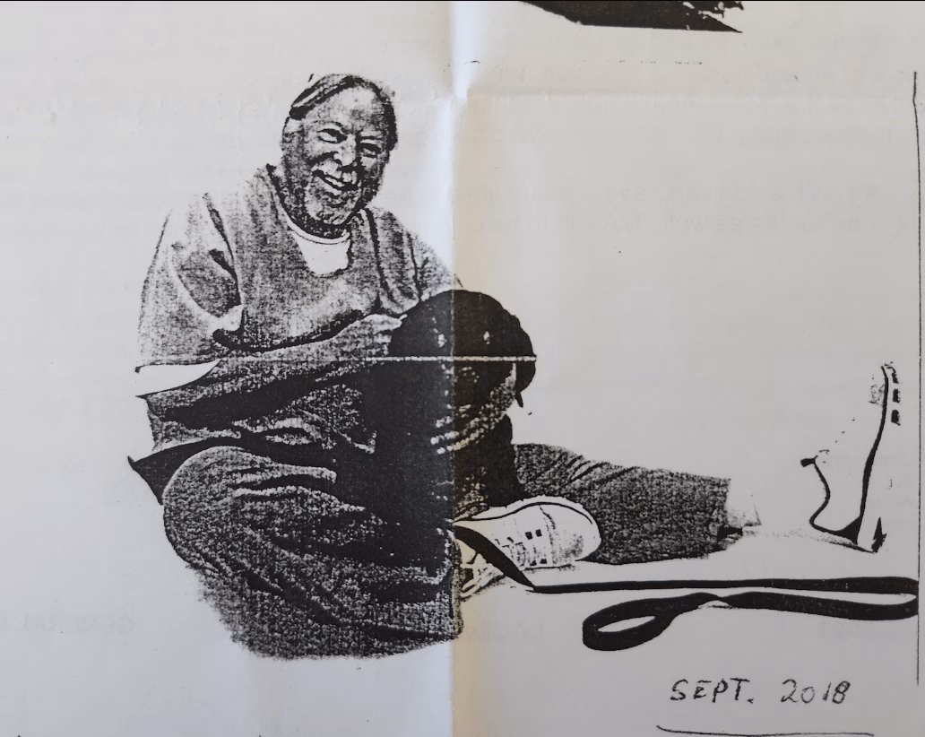 A black and white sketch of a smiling elderly woman sitting on the floor, holding a dark object, with a leash and a shoe nearby. The date "SEPT. 2018" is handwritten at the bottom right.