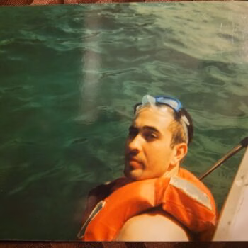 A man wearing an orange life vest and blue goggles on his head is in green water next to a boat.