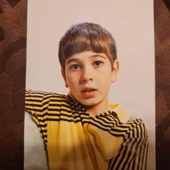 Portrait of a young boy with brown hair and a yellow and black striped shirt, looking directly at the camera.