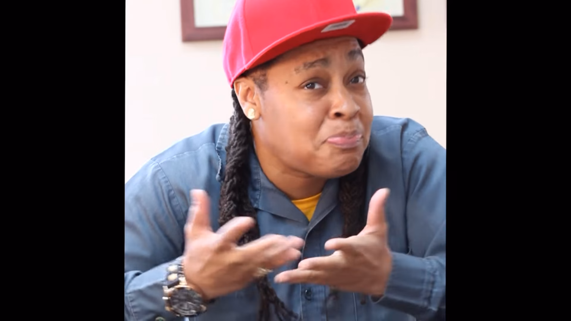Taliyah, wearing a red cap and blue shirt, gestures with both hands while speaking.