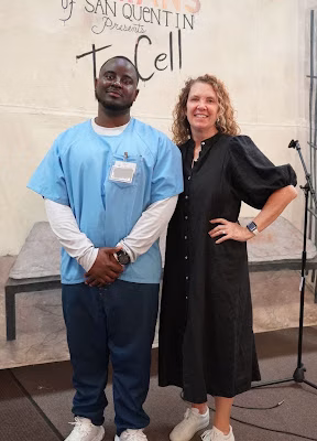 Eric and a woman posing for a photo in front of a 'Humans of San Quentin' banner.