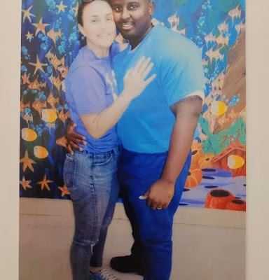 Eric4 and a woman posing together in front of a colorful mural.